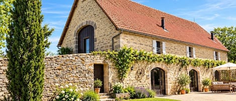 A stone house with a red-tiled roof, arched windows, and a well-maintained garden.