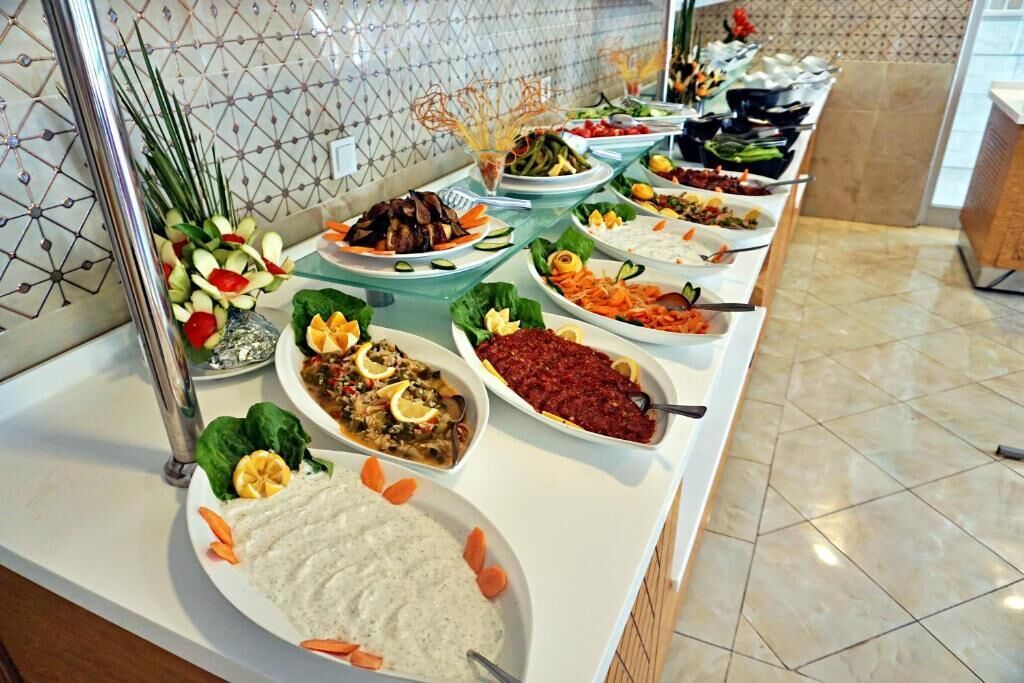 A buffet with various dishes, including salads, meats, and dips, arranged on a long table with a tiled backsplash.