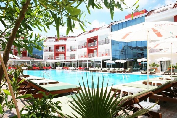 A hotel pool area with sun loungers, a Coca-Cola branded umbrella, and a glass building in the background.