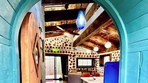 Un interior rústico con piso de madera, una puerta azul y un comedor con mesa y sillas.