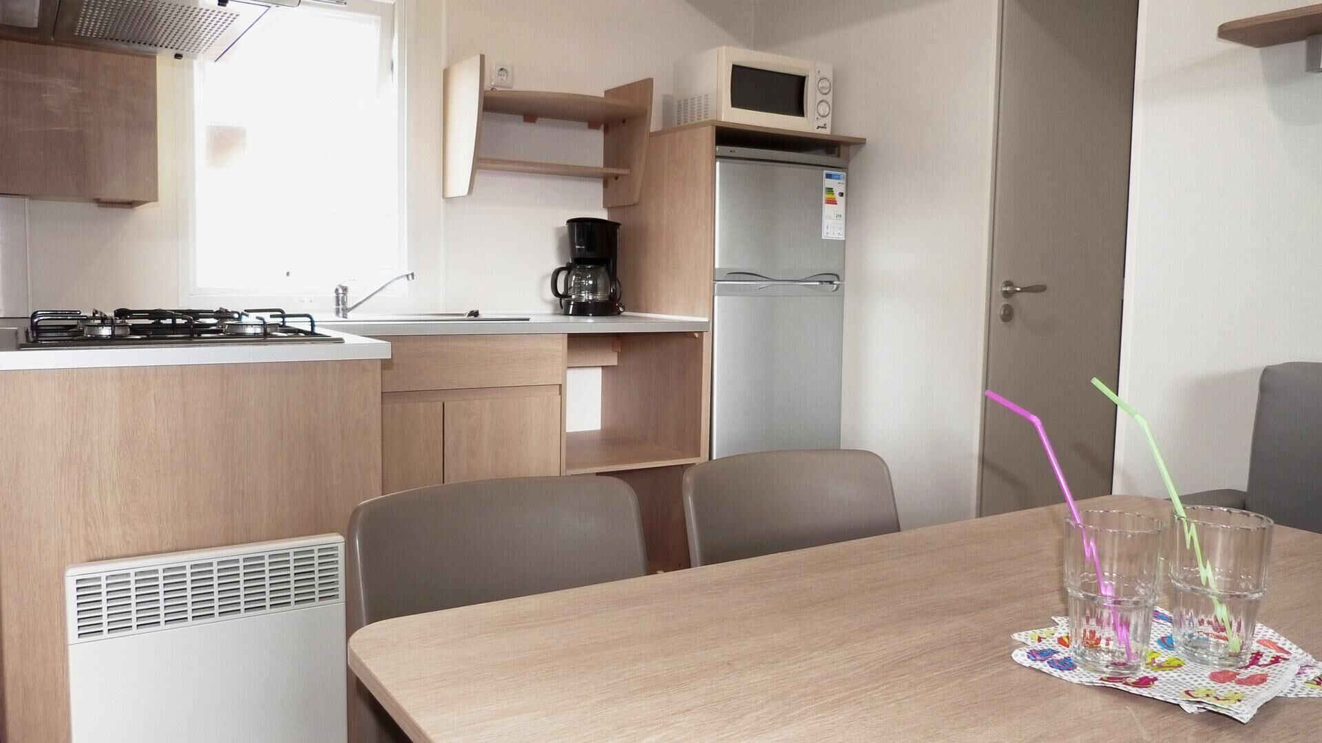 A compact kitchen with a gas stove, microwave, and coffee maker. There is a dining table with chairs and a small refrigerator.