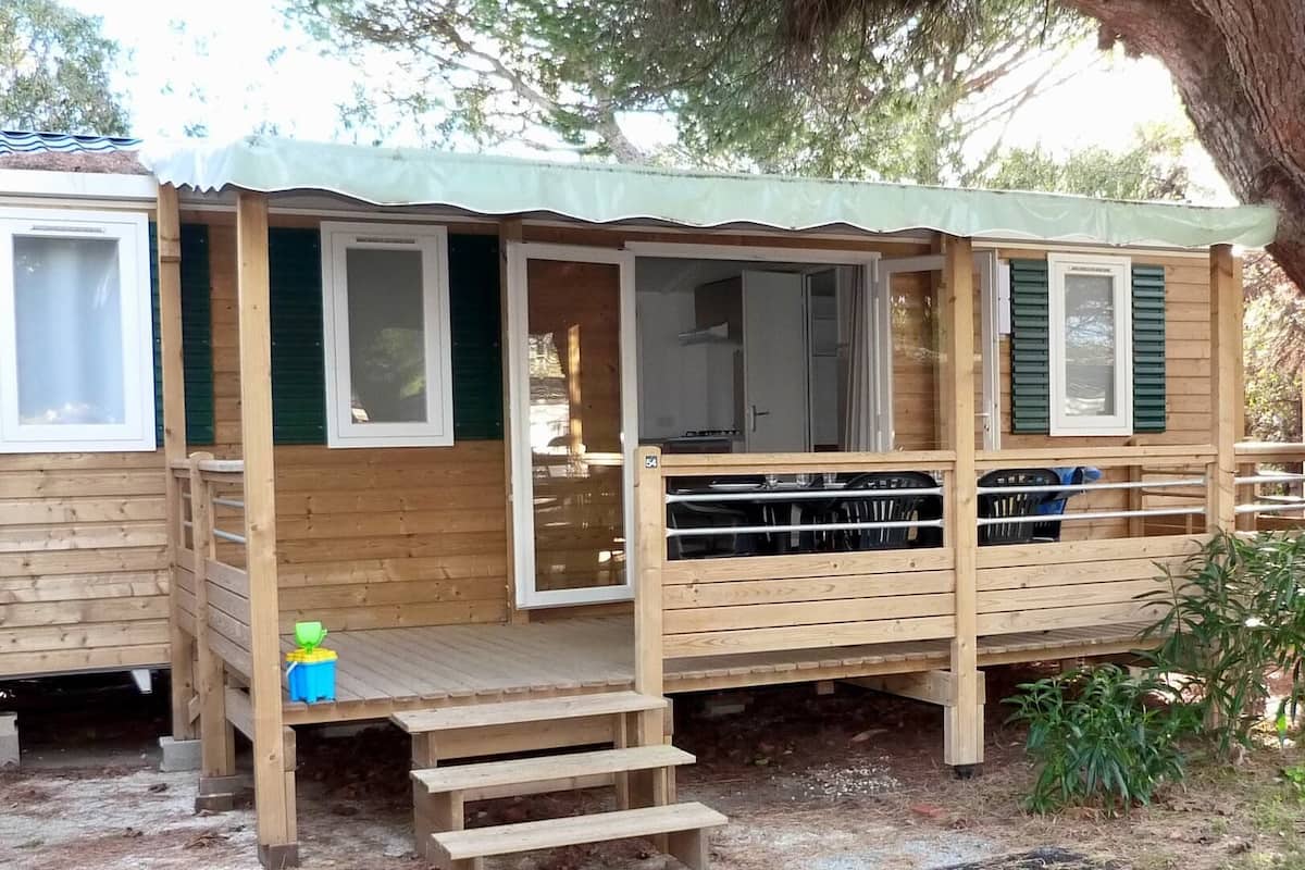 A wooden cabin with a deck, a covered porch, and a small outdoor seating area.