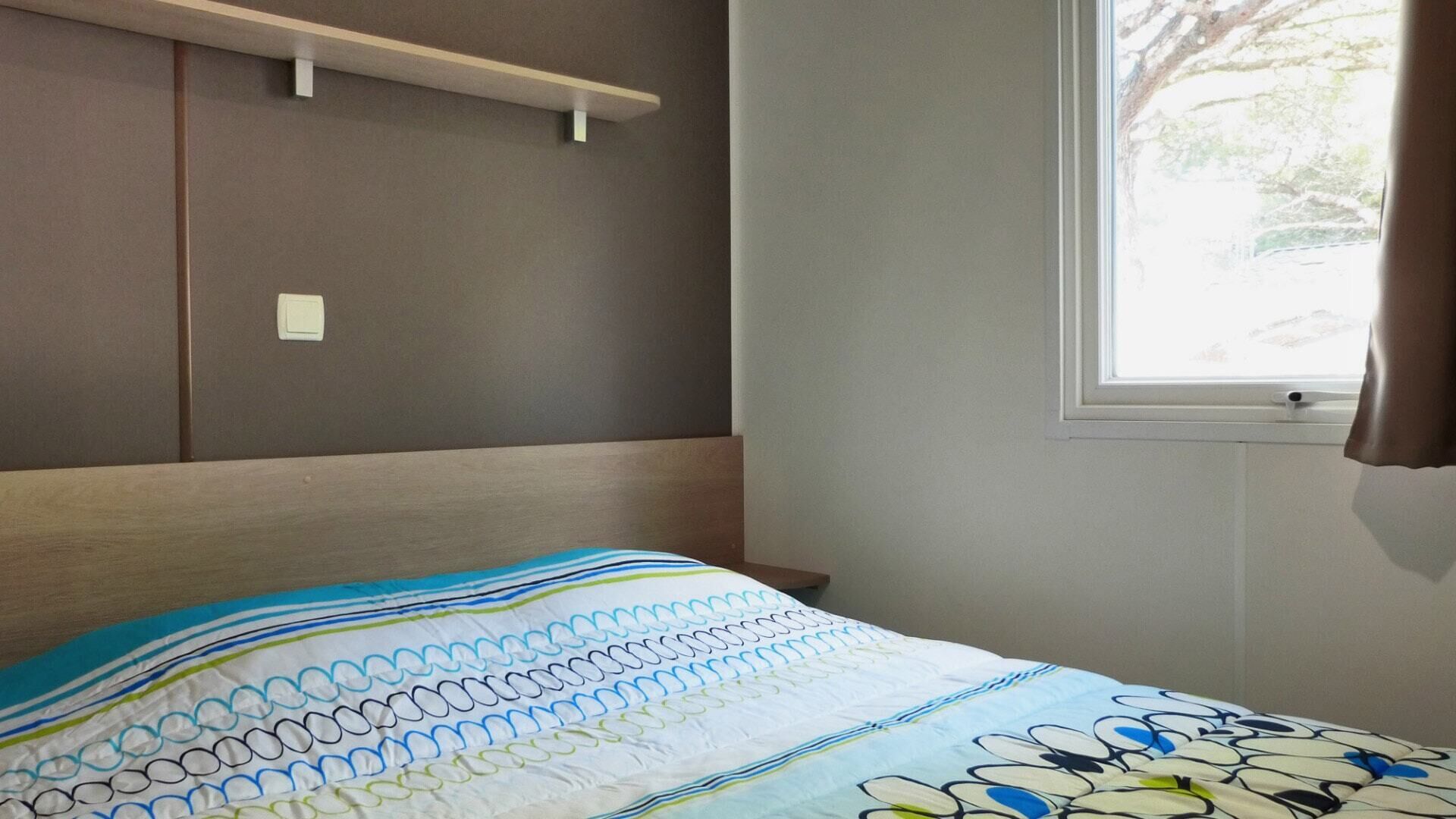 Un dormitori amb un llit, una finestra amb cortines i una estanteria penjada a la paret.