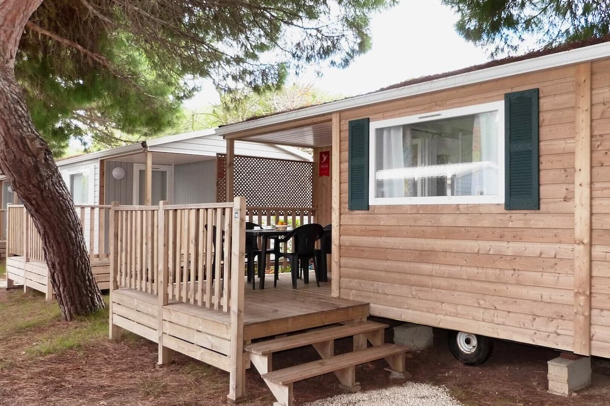 A mobile home with a wooden deck, a table, and chairs outside.