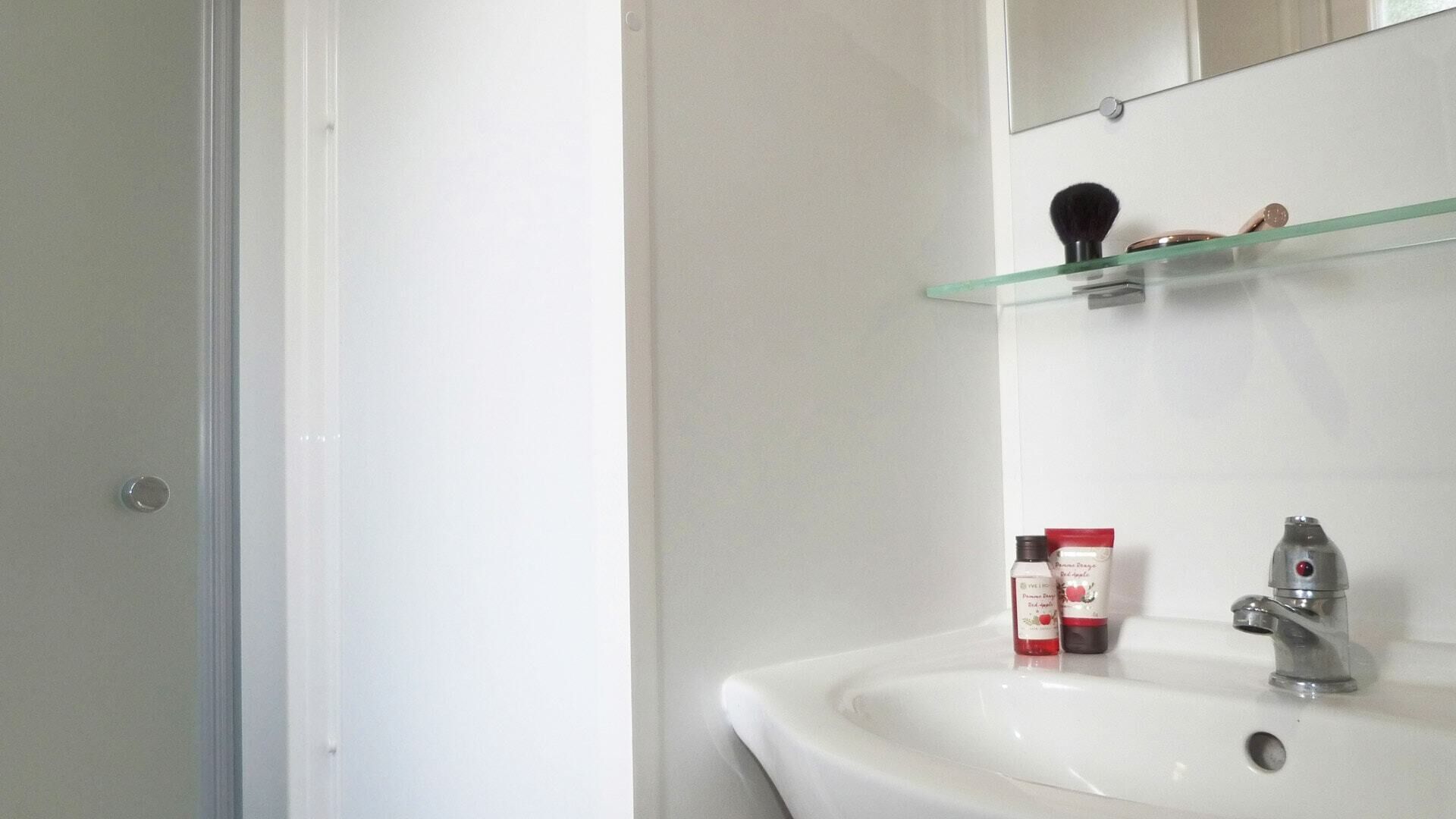 A bathroom with a white sink, a glass shelf above it, and a mirror.