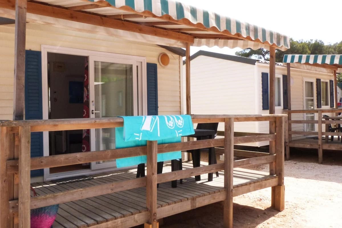A wooden deck with a covered seating area, a small table, and a window with blue shutters.