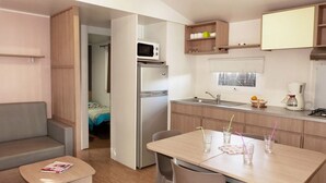 Una kitchenette compacta con microondas, refrigerador, lavamanos y cafetera. Incluye una mesa de comedor con sillas y una pequeña sala de estar con sofá.