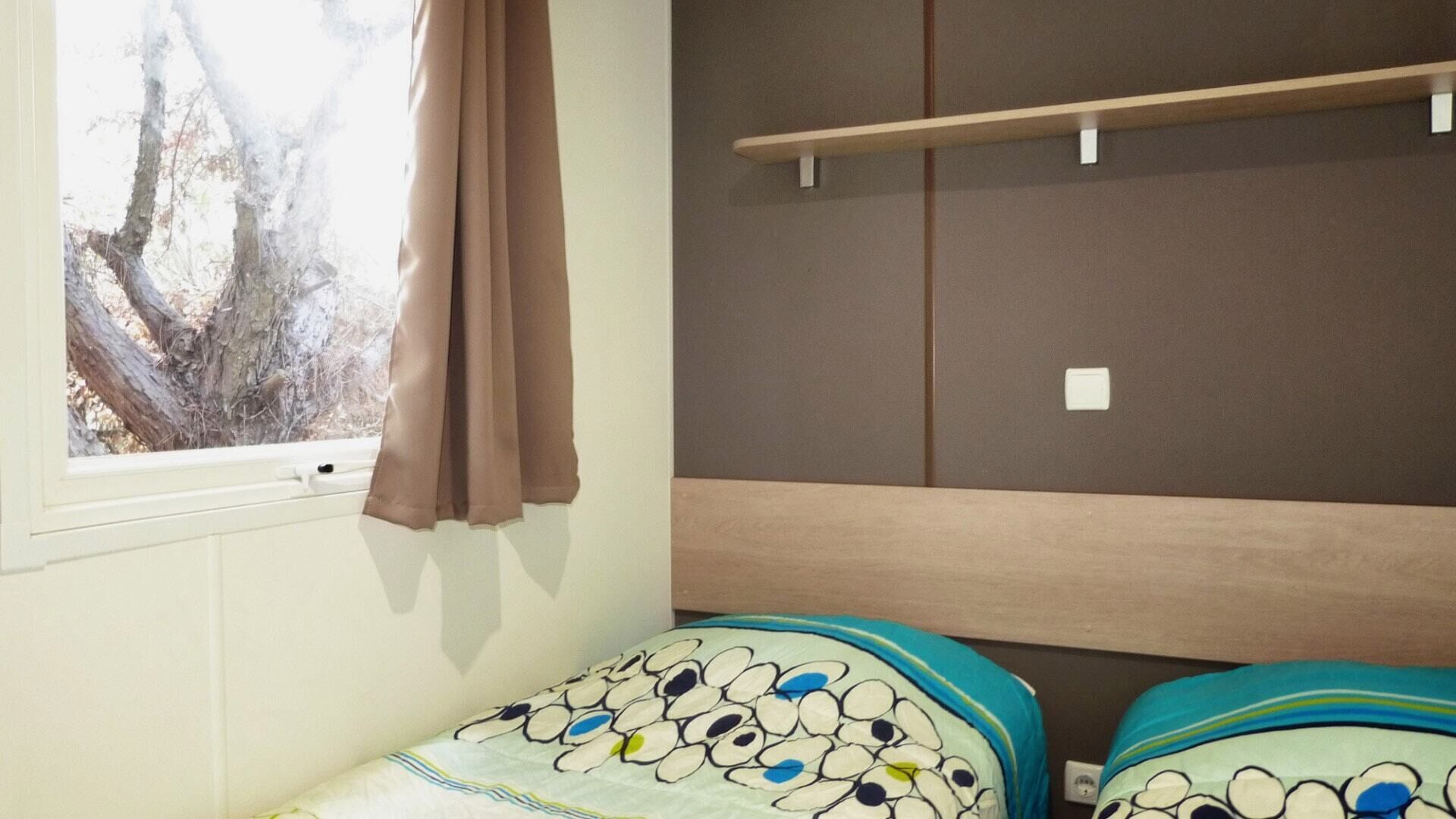 Ein Schlafzimmer mit Fenster, einem Bett mit gemustertem Kopfteil, einem Regal und einem an der Wand befestigten Lichtschalter.