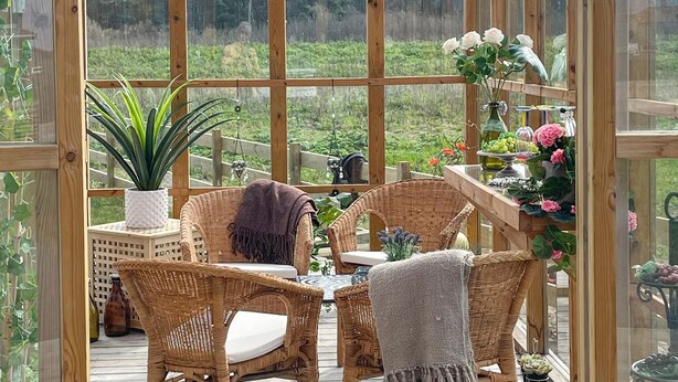 A glass-enclosed patio with wicker furniture, a potted plant, and a table with decorative items.