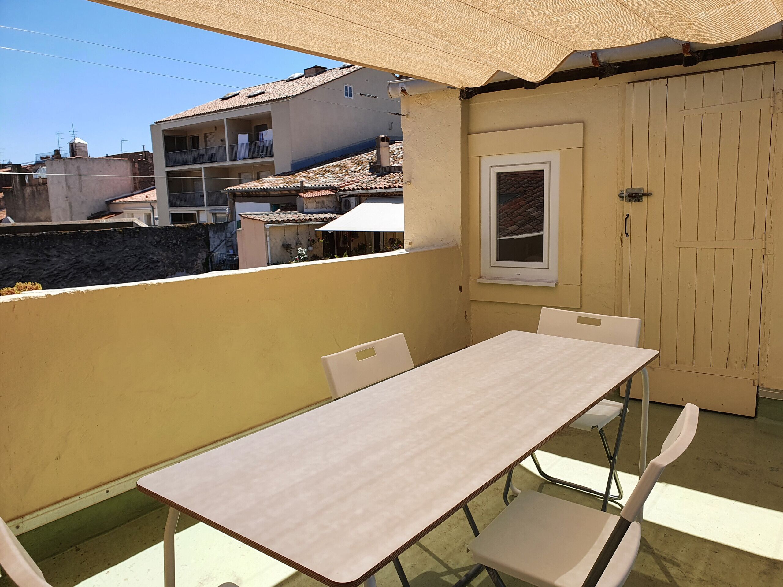Un balcon avec une table et des chaises, une porte et une fenêtre donnant sur un quartier résidentiel.