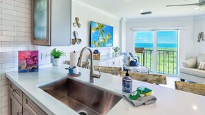 A modern kitchen with a large sink, a dining area with a view of the ocean, and a living room with a balcony. - Sunrise Oasis - Top Floor 2 BR 2 BA Condo  2411 (Tavernier)