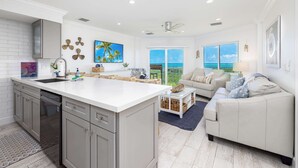 A modern kitchen with a large island, a dining area with a view, and a living room with a sofa and a coffee table. - Sunrise Oasis - Top Floor 2 BR 2 BA Condo  2411 (Tavernier)