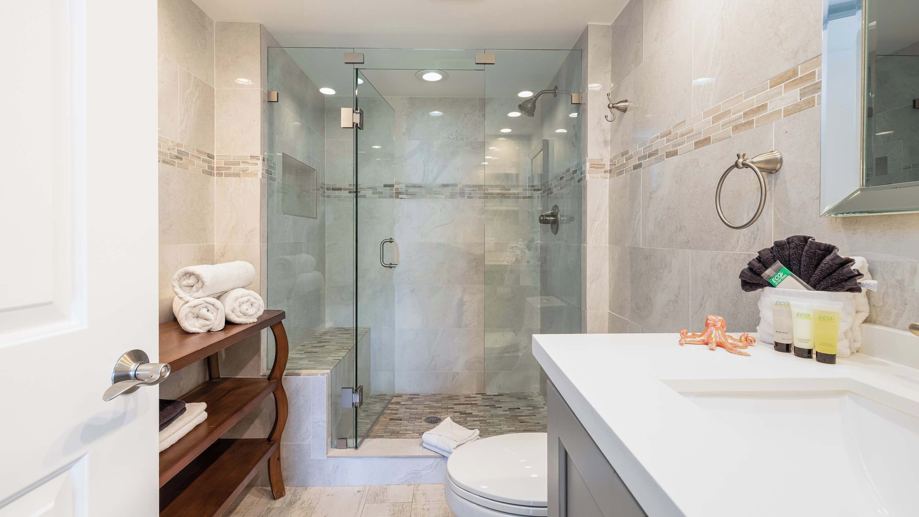 Une salle de bain moderne avec une douche à parois de verre, un lavabo blanc et un meuble-lavabo avec des articles de toilette.