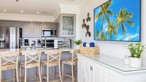 A modern kitchen with a dining area, featuring a large island with chairs, a microwave, and a coffee maker. - Sunrise Oasis | Top Floor | Ocean Pointe 2411 (Tavernier)