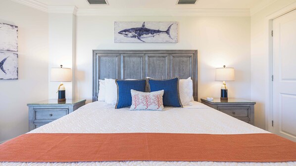 A neatly arranged bedroom with a large bed, two bedside tables with lamps, a wall-mounted artwork of a shark, and a door on the right.