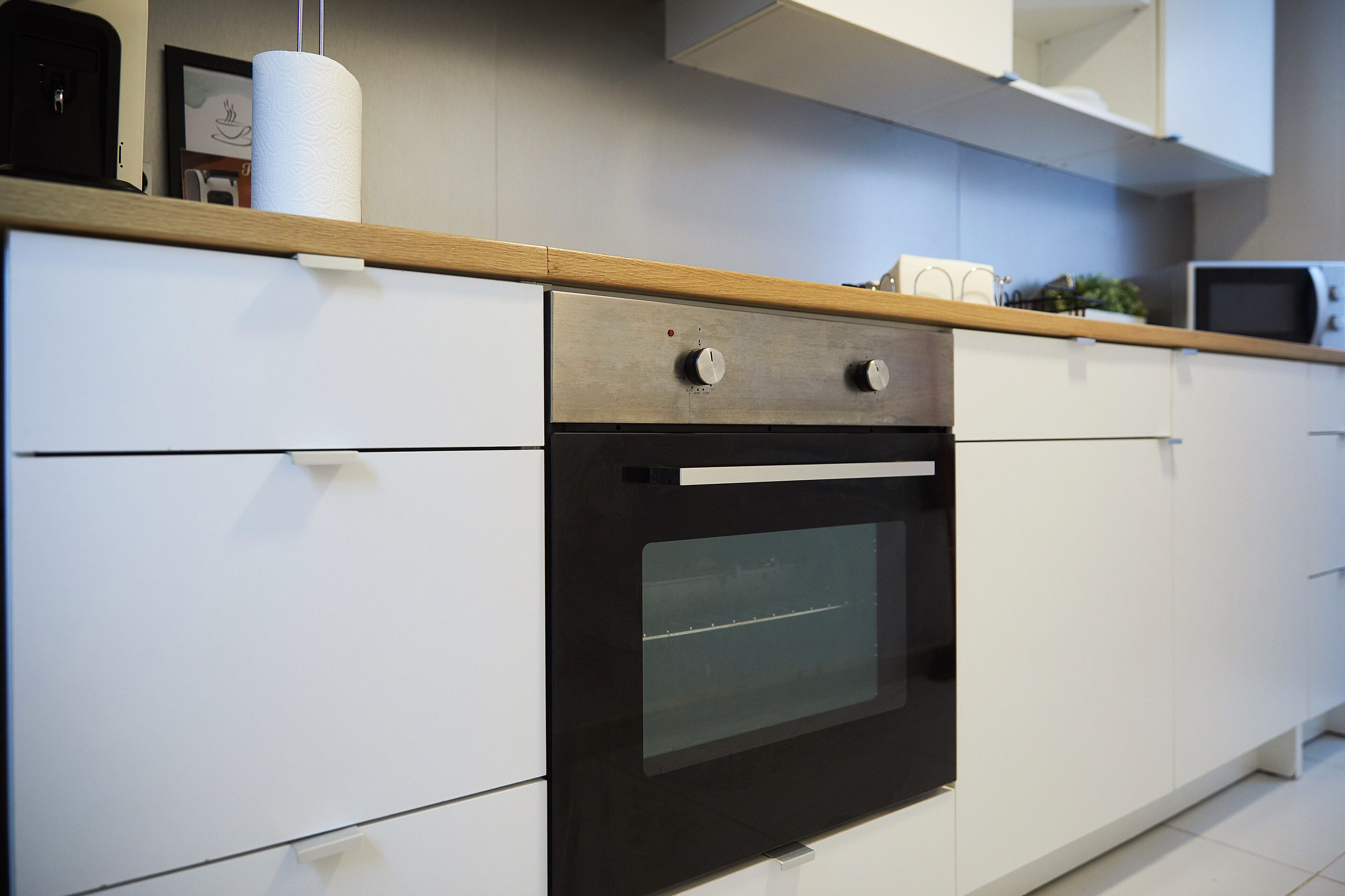 Une cuisine moderne avec des meubles blancs, un four en acier inoxydable et un plan de travail en bois.