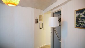 A hallway with white walls, a wooden floor, a hanging light fixture, and a door with a white lamp. - Family-sized apartments to spend quality time in Guimarães. (Guimarães)