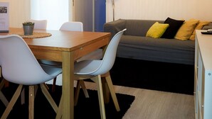 A modern living room with a wooden dining table, two white chairs, a grey sofa with yellow cushions, and a black rug. - Family-sized apartments to spend quality time in Guimarães. (Guimarães)
