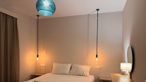 Habitación de hotel con una cama, dos lámparas de noche, un escritorio con lámpara, un espejo y una lámpara colgante azul.