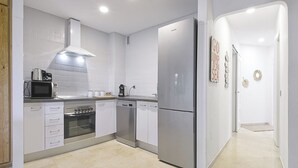 Una cuina moderna amb armaris blancs, un frigorífic d'acer inoxidable, un microones, un forn i un rentaplats.