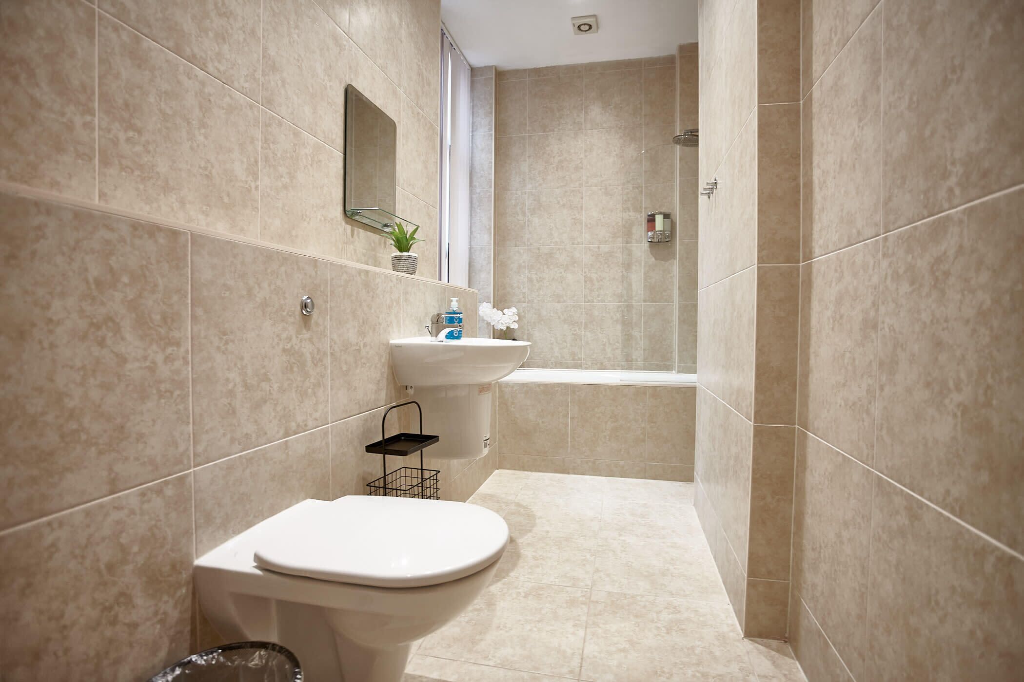 A modern bathroom with beige tiles, a white toilet, a sink with a mirror, and a shower area.
