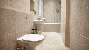 Ein modernes Badezimmer mit beigen Fliesen, einer weißen Toilette, einem Waschbecken mit Spiegel und einer Duschkabine.