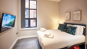 Ein Hotelzimmer mit Bett, Fernseher, Fenster mit Vorhängen und Bildern an der Wand.