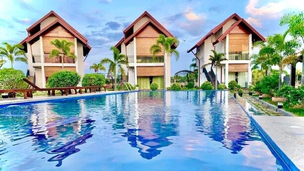 A swimming pool with two buildings on either side, surrounded by greenery.
