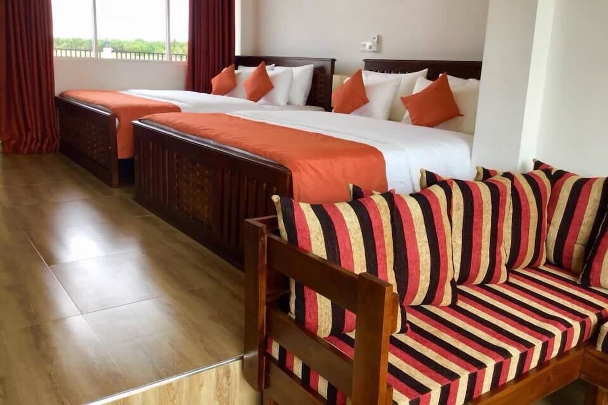 Habitación de hotel con dos camas, un sofá y vistas al exterior con vegetación.