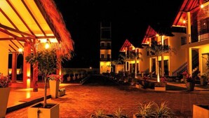 A courtyard with thatched-roof buildings, a central staircase, and potted plants.