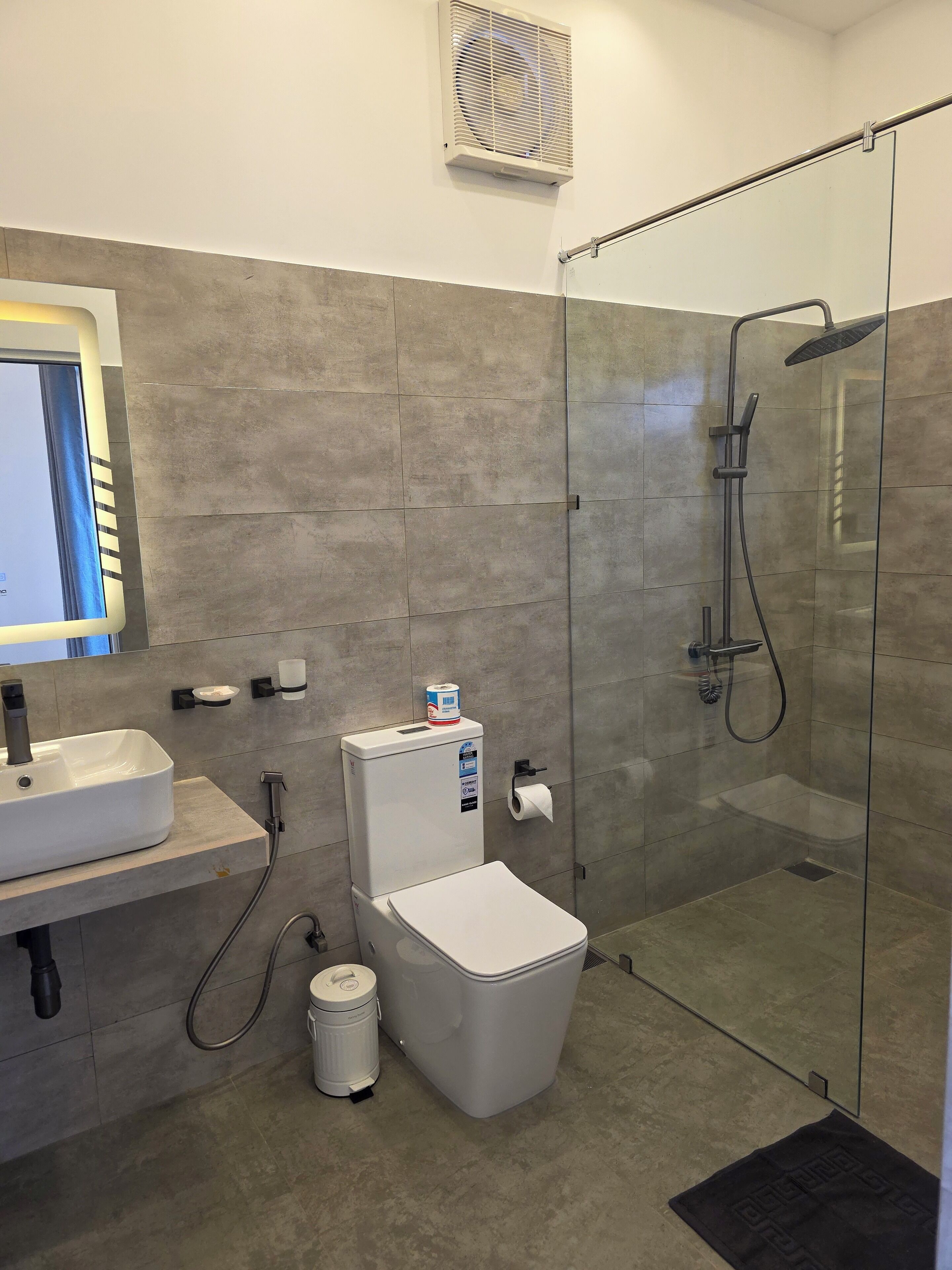 A modern bathroom with a glass-enclosed shower, a white toilet, a sink, and a toilet paper holder.