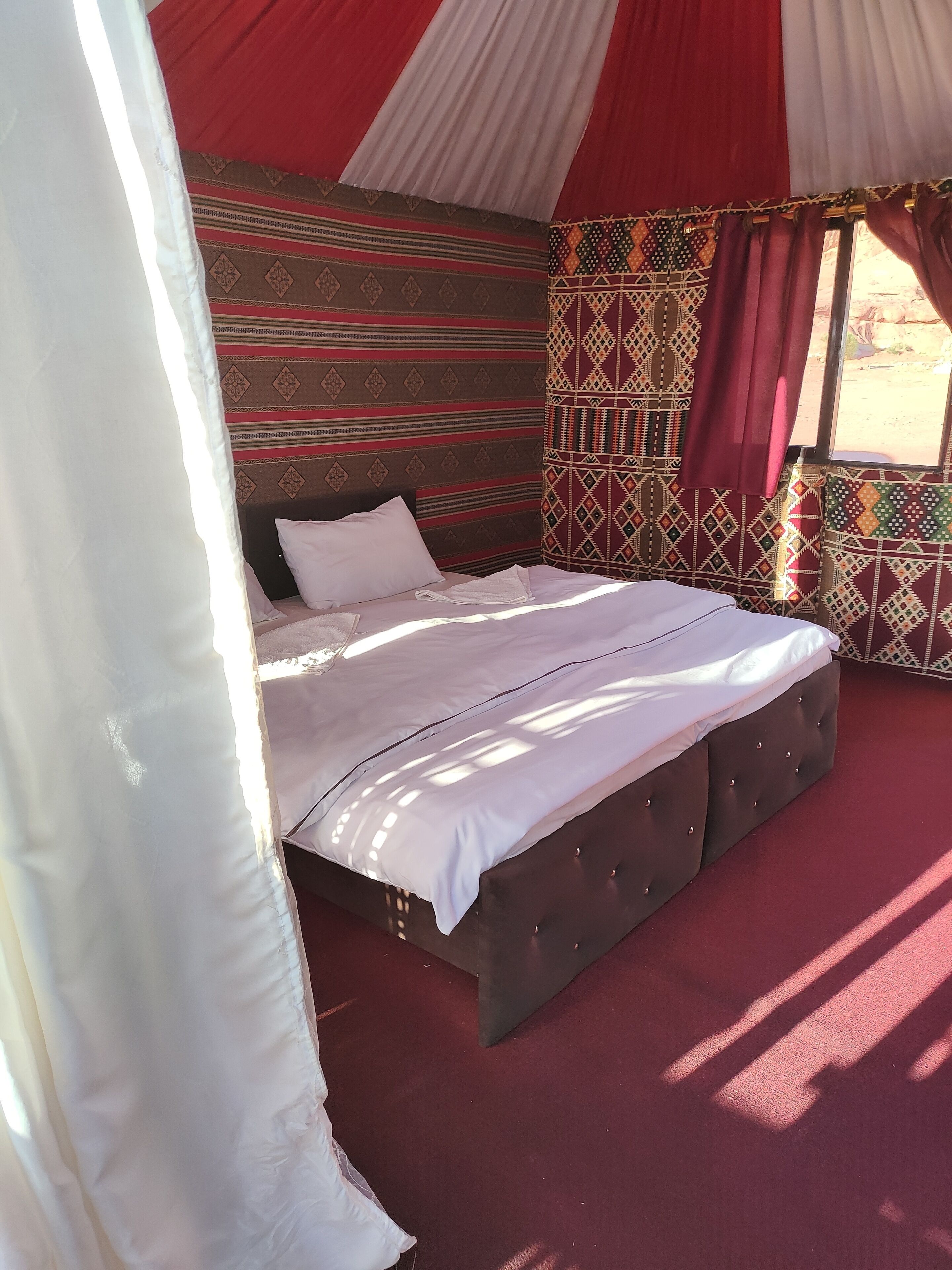A bed with a white comforter and pillows, a tufted headboard, and a patterned wall.