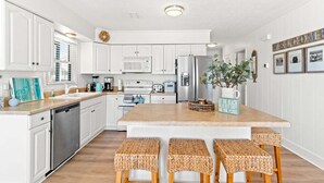 Una cocina moderna con armarios blancos, una isla central con taburetes, electrodomésticos de acero inoxidable y una guirnalda decorativa en el techo.