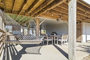 Un espace extérieur abrité, aménagé avec un hamac, des chaises en bois et une table.