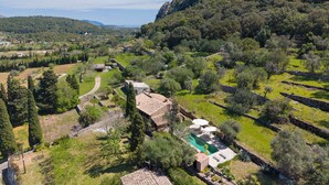 A villa with a swimming pool, surrounded by lush greenery and a mountainous backdrop. - Finca Es Coste by Rentallorca (Pollensa)