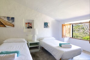 A room with two single beds, a nightstand with a lamp, and a window with a view of greenery. - Finca Es Coste by Rentallorca (Pollensa)