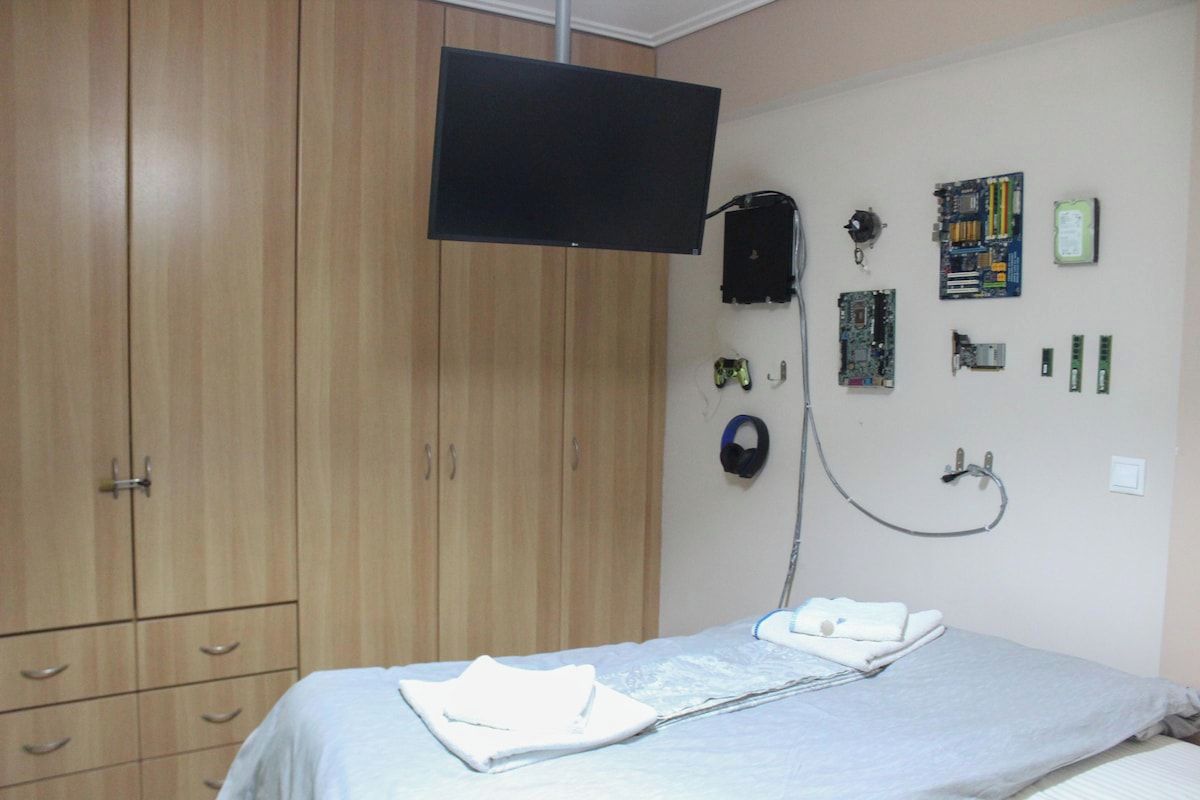 A bedroom with a bed, a television mounted on the wall, a wardrobe, and various electronic devices and accessories.