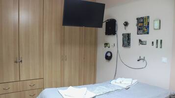 A bedroom with a bed, a television mounted on the wall, a wardrobe, and various electronic devices and accessories.