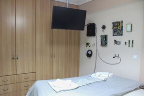 Ein Schlafzimmer mit einem Bett, einem an der Wand befestigten Fernseher, einem Kleiderschrank und verschiedenen elektronischen Geräten und Zubehör.