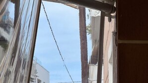 Blick durch ein Fenster mit Vorhang, der ein mehrstöckiges Gebäude und einen klaren Himmel zeigt.