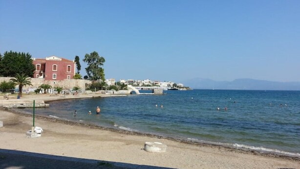 Eine Küstenlandschaft mit Sandstrand, einer Steinbrücke und Gebäuden im Hintergrund.