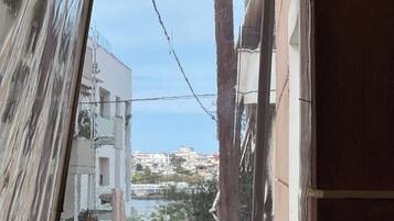 A window with a view of a coastal town, a tree, and a building with a balcony.
