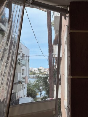 Una ventana con vista a un pueblo costero, un árbol y un edificio con balcón.