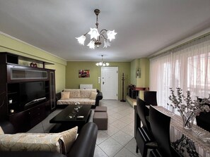 A living room with a television, sofa, coffee table, and a dining area with a table and chairs.