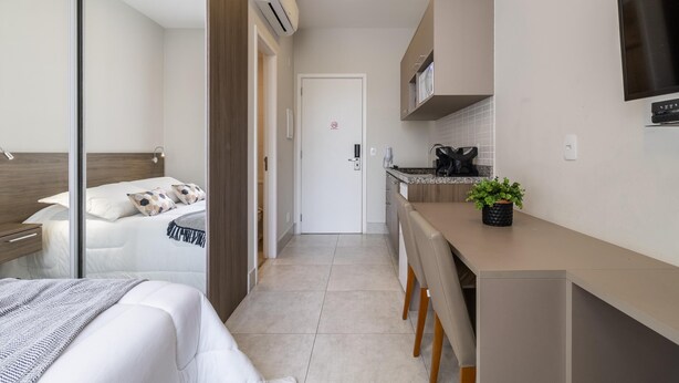 A modern hotel room with a bed, bedside table, and a small kitchenette.