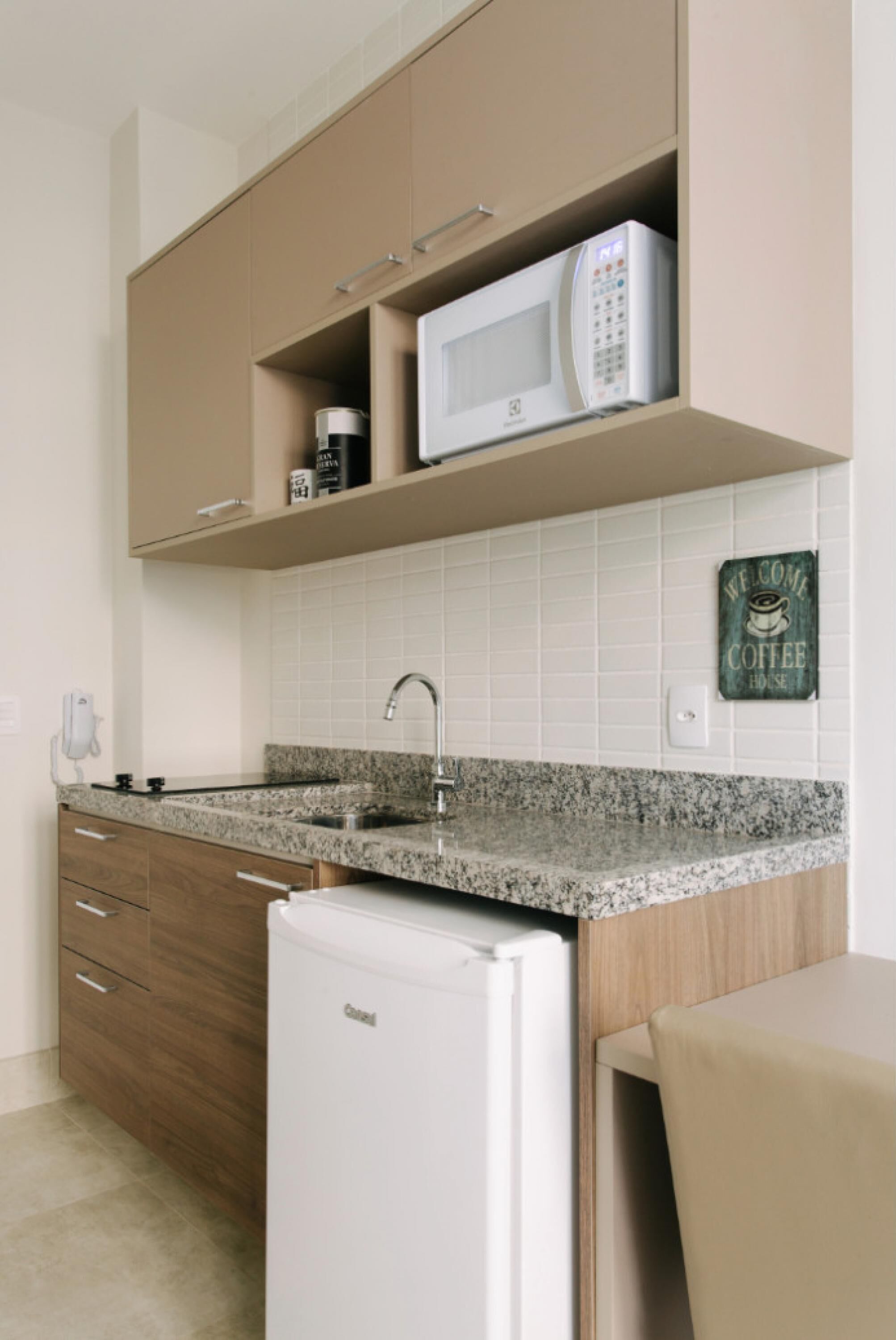 A modern kitchen with a built-in microwave, a coffee sign, and a refrigerator.