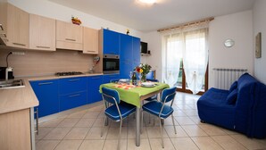 A modern kitchen with blue cabinets, a dining table with chairs, and a blue sofa in a bright living area. - Casa Blu (Toscolano Maderno)