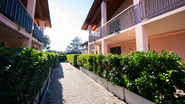 A pathway flanked by neatly trimmed hedges and a building with balconies. - Casa Blu (Toscolano Maderno)