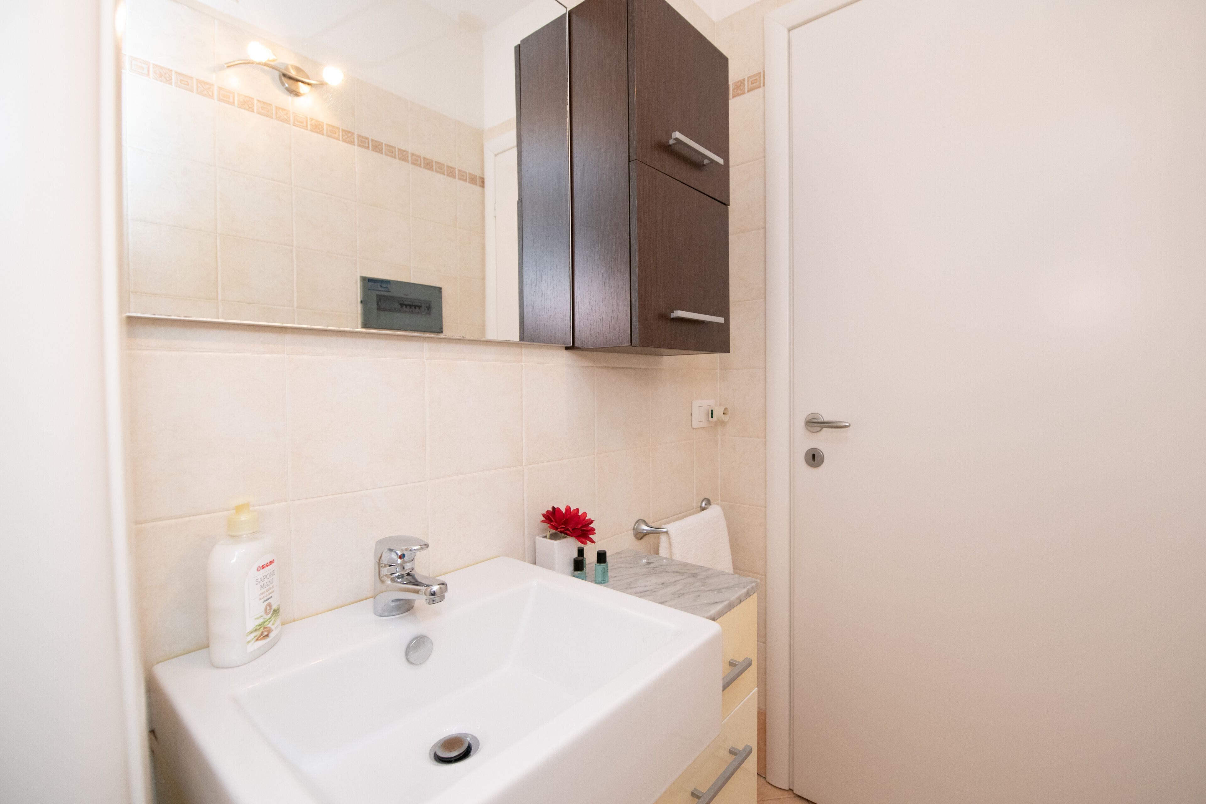 Une salle de bain avec un lavabo blanc, un miroir, un meuble en bois foncé et une serviette suspendue à un porte-serviettes.
