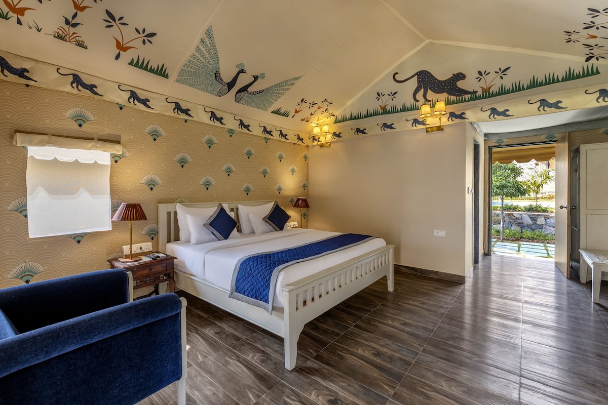 Une chambre à coucher comprenant un lit, des tables de chevet, une chaise et une fresque murale au plafond représentant des motifs d’animaux.